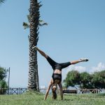 A woman enjoying a cartwheel on a grassy park under clear blue skies, surrounded by palm trees.