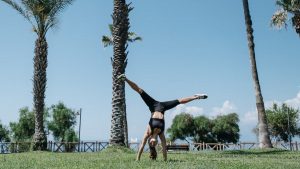A woman enjoying a cartwheel on a grassy park under clear blue skies, surrounded by palm trees.